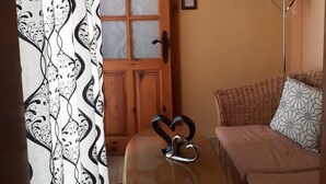 A cozy room with a wooden door, a patterned curtain, a small table with a heart-shaped object, a sofa, and a floor lamp. - Nocturne Family House (Paola)