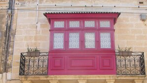 A building with a red door labeled "Nefame," a red window with decorative glass, and a balcony with wrought iron railings. - Nocturne Family House (Paola)