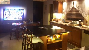 A kitchen with a dining table, chairs, a television, and a counter with various items. - Nocturne Family House (Paola)
