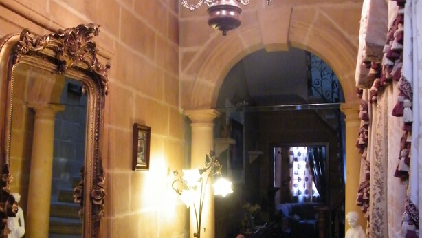 A hallway with a large ornate mirror, a chandelier, and classical architecture including columns and an arched doorway. - Nocturne Family House (Paola)