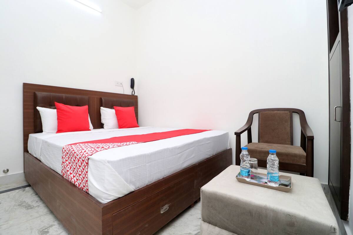A neatly made bed with a red and white bedspread, a wooden headboard, and a bedside table with two water bottles.