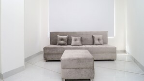 Una sala de estar moderna con un sofá y reposapiés grises, un ventanal grande y una pared blanca.
