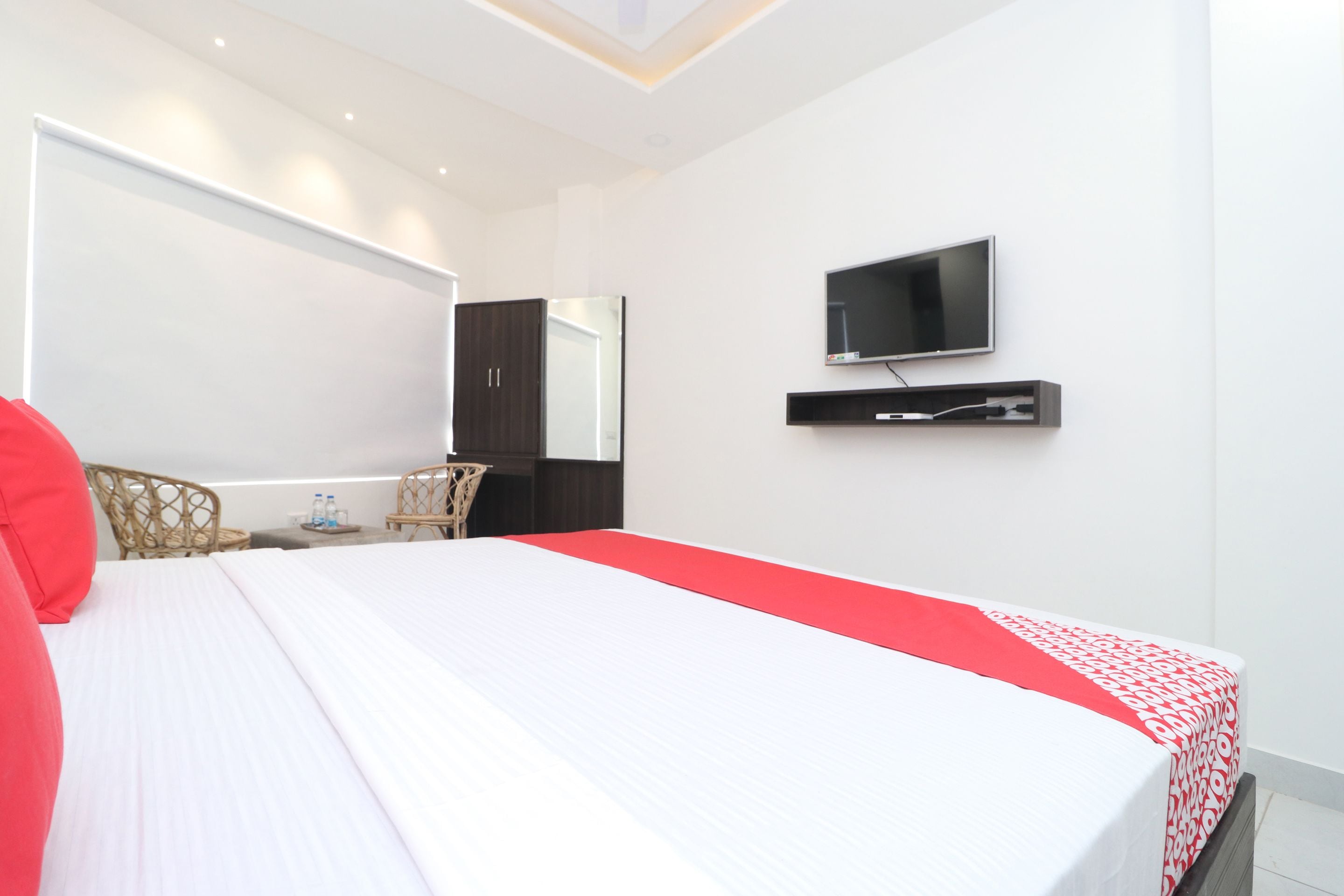 Quarto de hotel moderno com uma cama grande, televisão de tela plana na parede e uma pequena área de estar com uma poltrona e mesa.