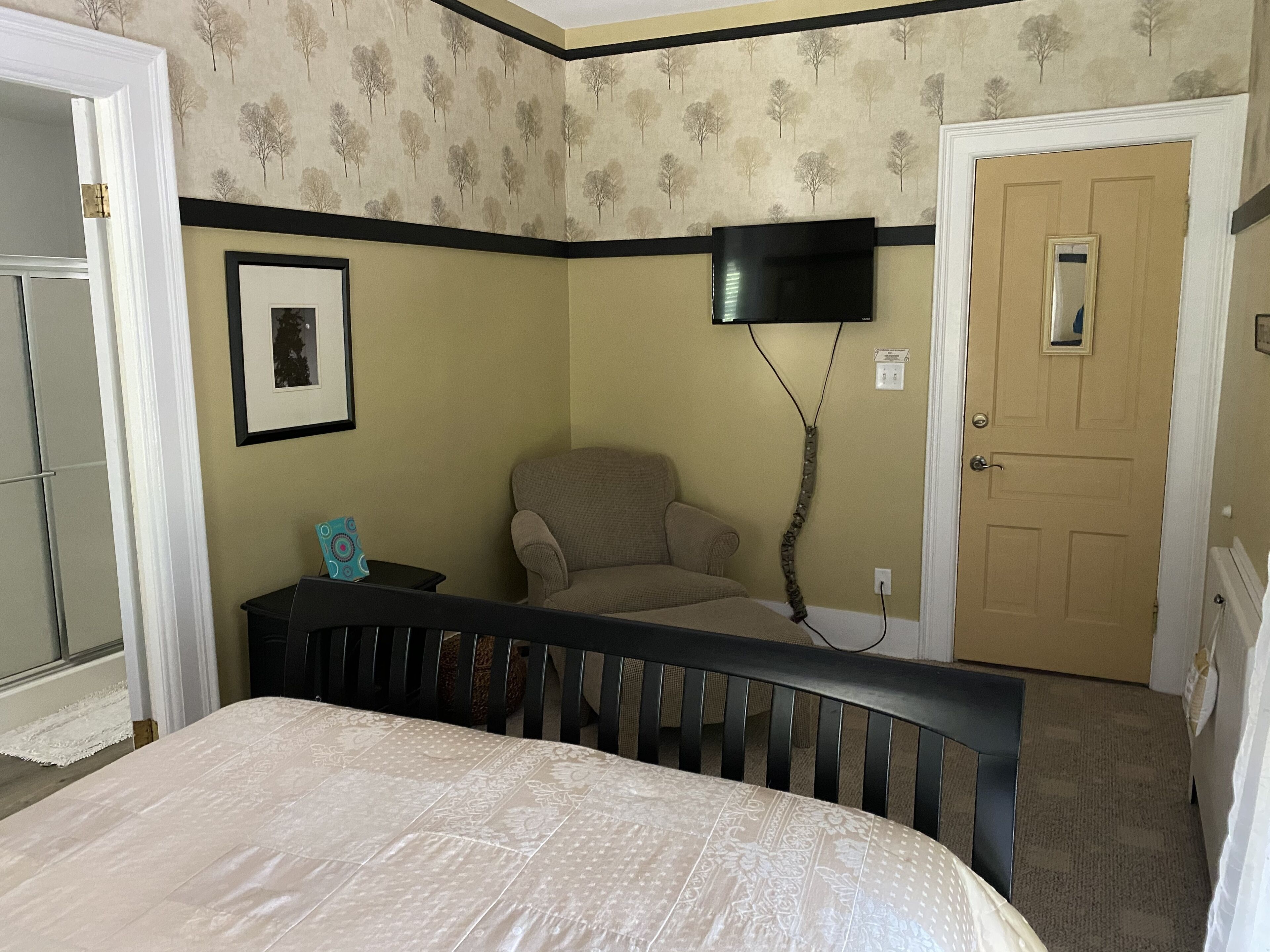 A bedroom with a bed, a chair, a television mounted on the wall, and a door.