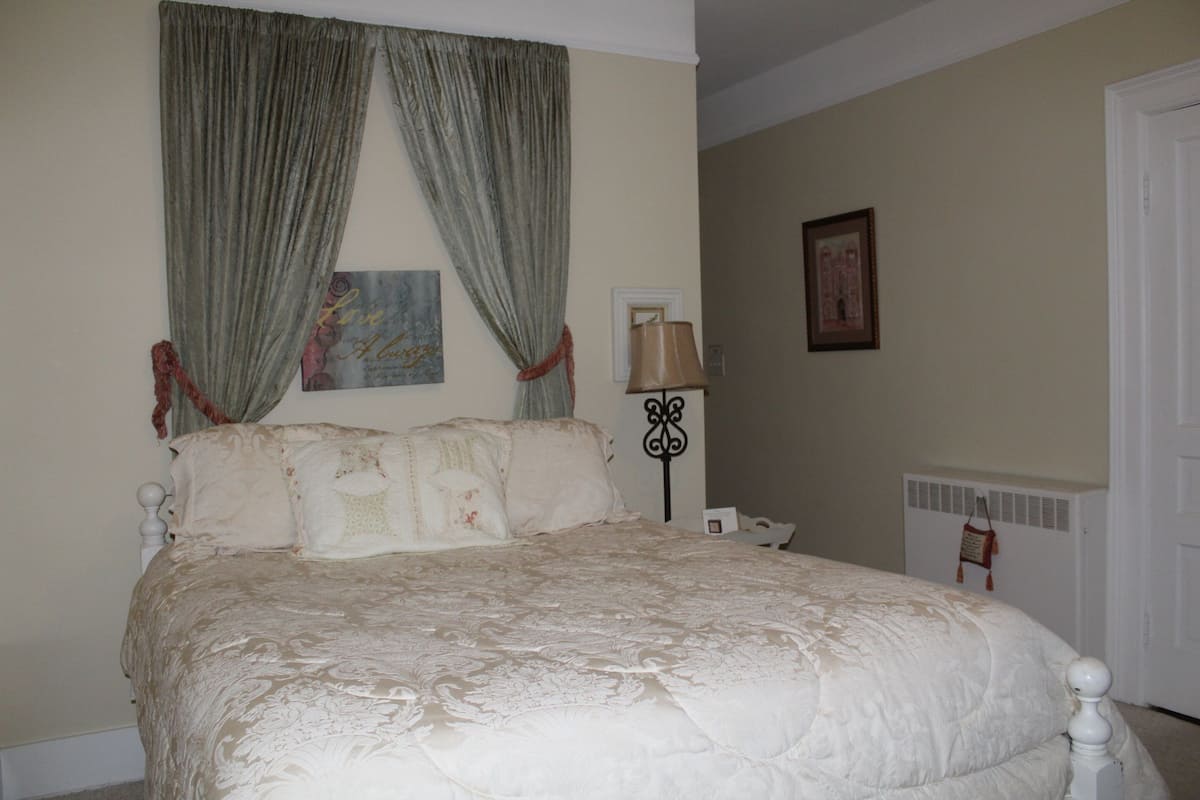 Une chambre à coucher avec un grand lit, une table de chevet, une lampe et un tableau encadré au mur.