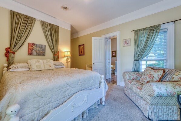 A bedroom with a large bed, a sofa, and a door leading to another room.