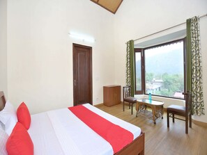 A bedroom with a bed, a wooden wardrobe, a small table with chairs, and a window with a view of the outdoors. - OYO Home 13529 Exotic 3BHK (Kasauli)