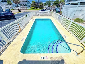 Una piscina rectangular amb un indicador de profunditat de 3 peus, envoltada per una tanca blanca i un senyal de socorrista que indica que no es permet submergir.