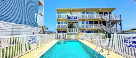 A swimming pool with a 5 FT depth marker, surrounded by a white fence with 'SHALLOW WATER NO DIVING ALLOWED' signs, and a building labeled 'GRAND STRAND RESORT II' in the background.