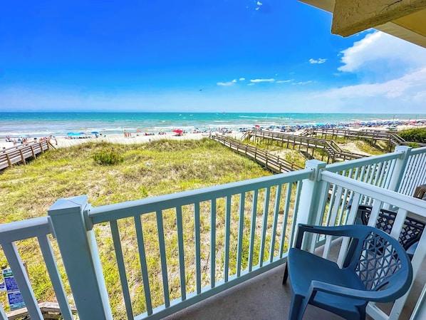 A balcony with a view of a beach, a wooden fence, and a chair.