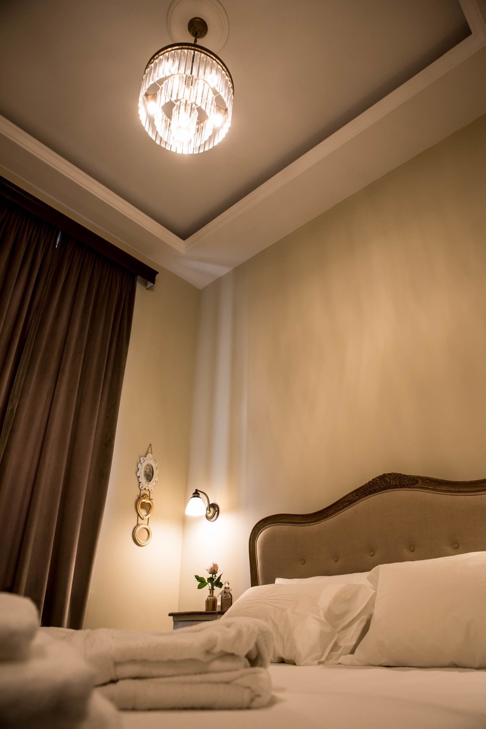 Une chambre d’hôtel avec un grand lit, un lustre, une table de chevet avec une lampe et un miroir fixé au mur.