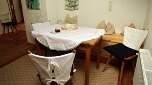 Zona pranzo con tavolo apparecchiato per due, una sedia con copertina bianca e una panca di legno con cuscini.
