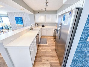 A modern kitchen with white cabinetry, stainless steel appliances, and a wooden floor.
