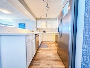 A modern kitchen with white cabinetry, stainless steel appliances, and a wooden floor.