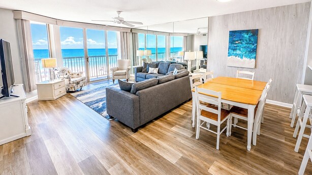 A spacious living area with a large sofa, a dining table, and a view of the ocean through large windows.