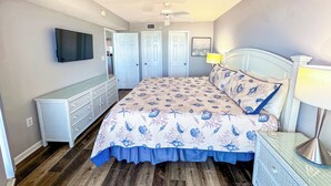 A bedroom with a bed, dresser, TV, and doors.