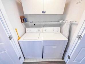 A laundry room with two white washing machines, a shelf above, and a towel rack. - Emerald Cove II 4B (North Myrtle Beach)