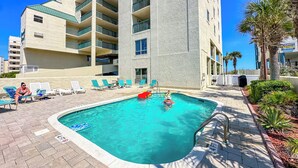 A swimming pool area with lounge chairs and a tall building in the background.