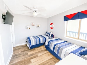 A bedroom with two beds, a ceiling fan, a TV, and a window with a view. - Emerald Cove II 4B (North Myrtle Beach)