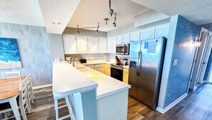 A modern kitchen with white cabinets, stainless steel appliances, and a wooden dining table.