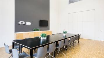 Un salón de conferencias con una larga mesa, sillas grises, un televisor de pantalla plana y suelo de madera.