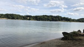 A calm lake with a sandy shore and a forested hill in the background.