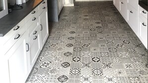 A kitchen with white cabinets, a stone wall, a brick oven, and patterned floor tiles.