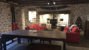 A rustic stone-walled room with a wooden table, red sofas, and a fireplace.