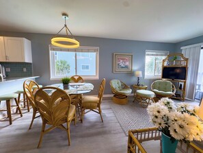 A dining area with wicker chairs, a round table, and a hanging light fixture.
