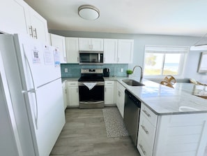 A modern kitchen with white cabinets, a stainless steel refrigerator, a microwave, a stove, and a dishwasher.