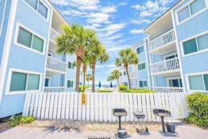 A beachfront hotel with multiple balconies, palm trees, and barbecue grills.