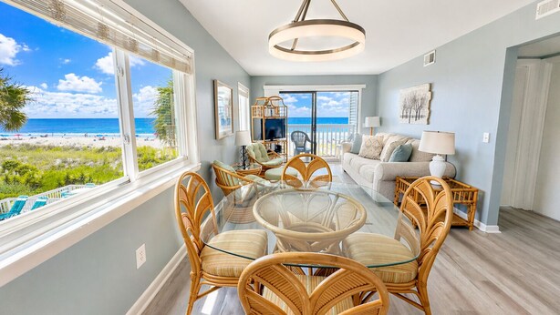 A room with a glass table surrounded by wicker chairs, a sofa, and a view of the beach. - Charming Oceanfront Escape – 2BR/2BA at Ocean Garden Villas #L2 (North Myrtle Beach)