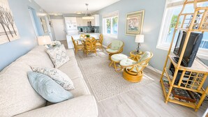 A living room with a sofa, chairs, a dining table, and a TV stand. - Charming Oceanfront Escape – 2BR/2BA at Ocean Garden Villas #L2 (North Myrtle Beach)