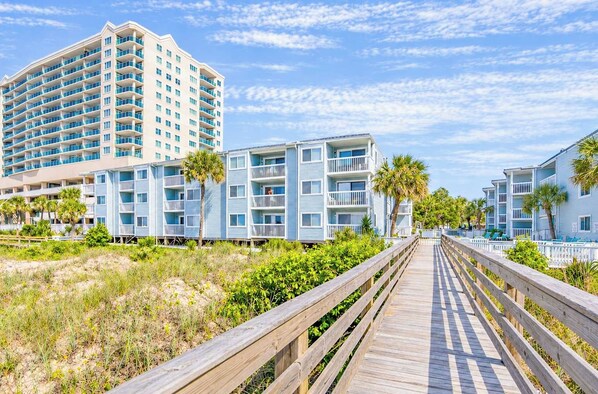 A coastal hotel with multiple-story buildings, a wooden boardwalk, and palm trees.