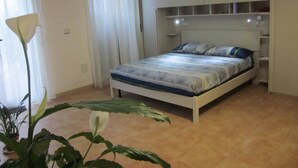 Une chambre à coucher avec un lit, une table de chevet, une plante en pot et une fenêtre avec des rideaux.