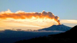 Une montagne dont le sommet est surmonté d’un panache de fumée, entourée de nuages.
