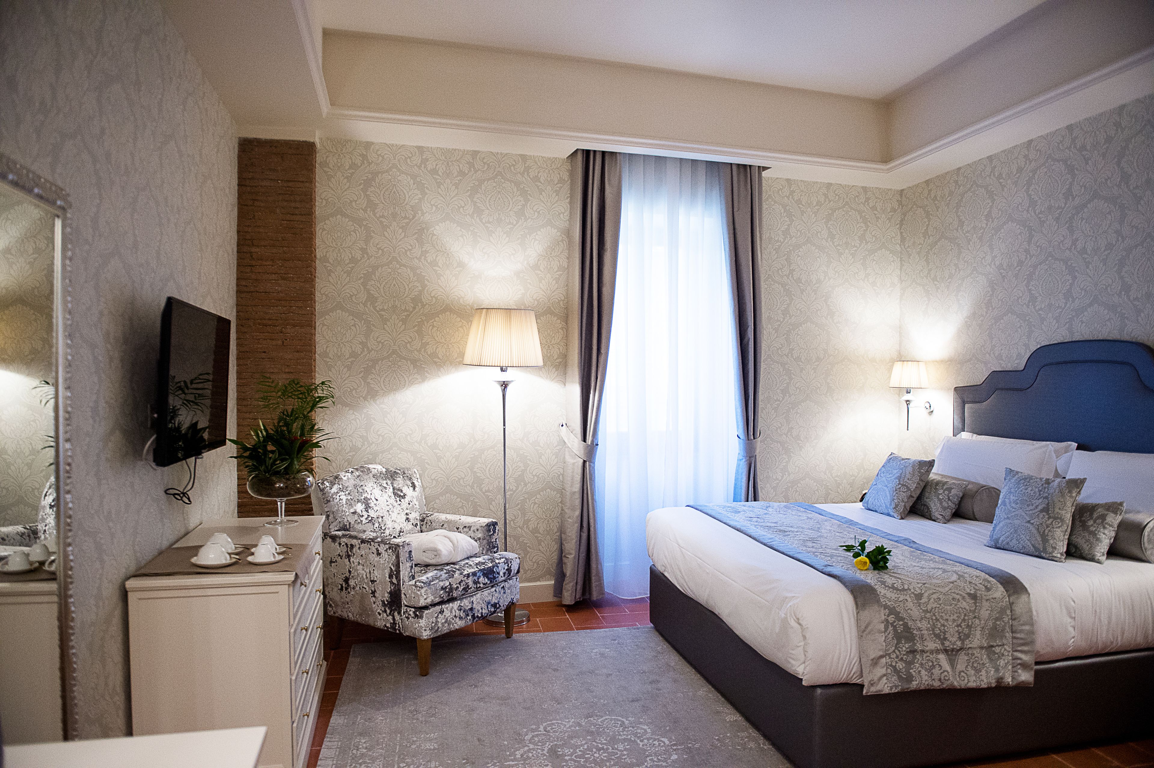 A hotel room with a bed, a chair, a desk, a lamp, and a window with curtains.