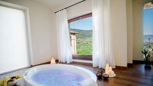 Habitación de spa con hidromasaje, frutero, velas y vistas a un puente y colinas.