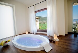 Habitación de spa con hidromasaje, frutero, velas y vistas a un puente y colinas.