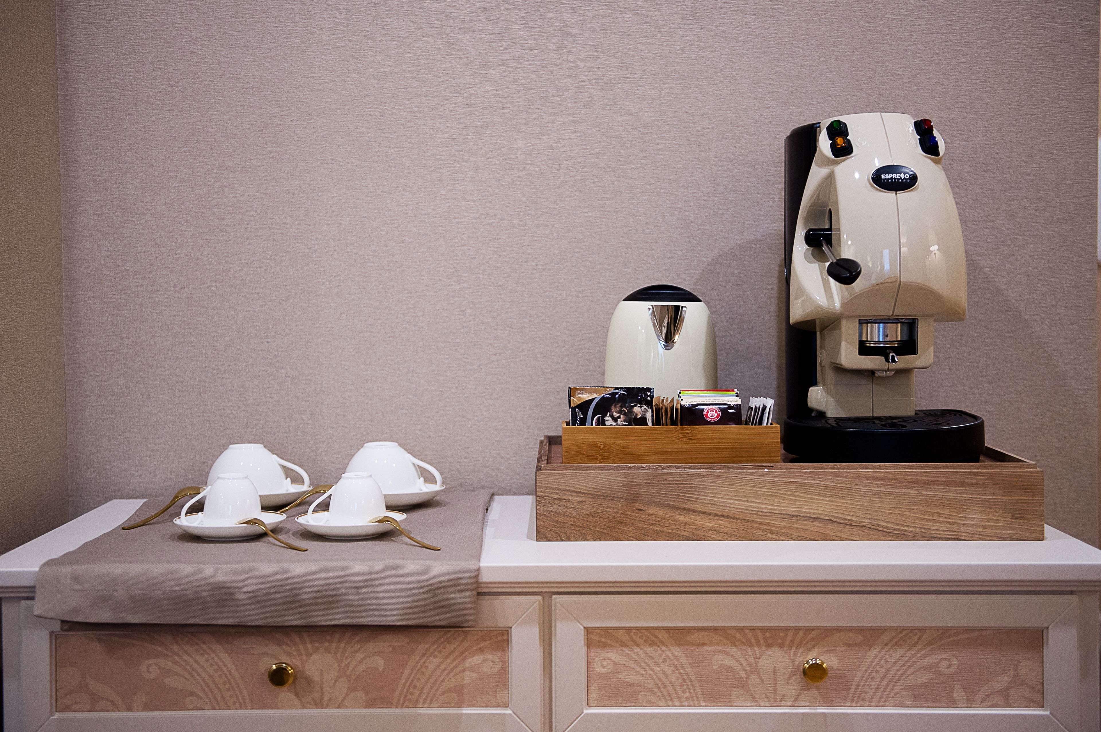 A coffee machine on a wooden tray with a coffee pot and cups on a table.