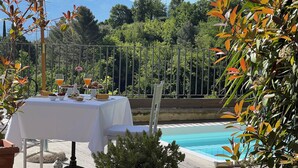 Zona de comedor junto a la piscina con una mesa para dos, un vaso de jugo de naranja y una planta pequeña.