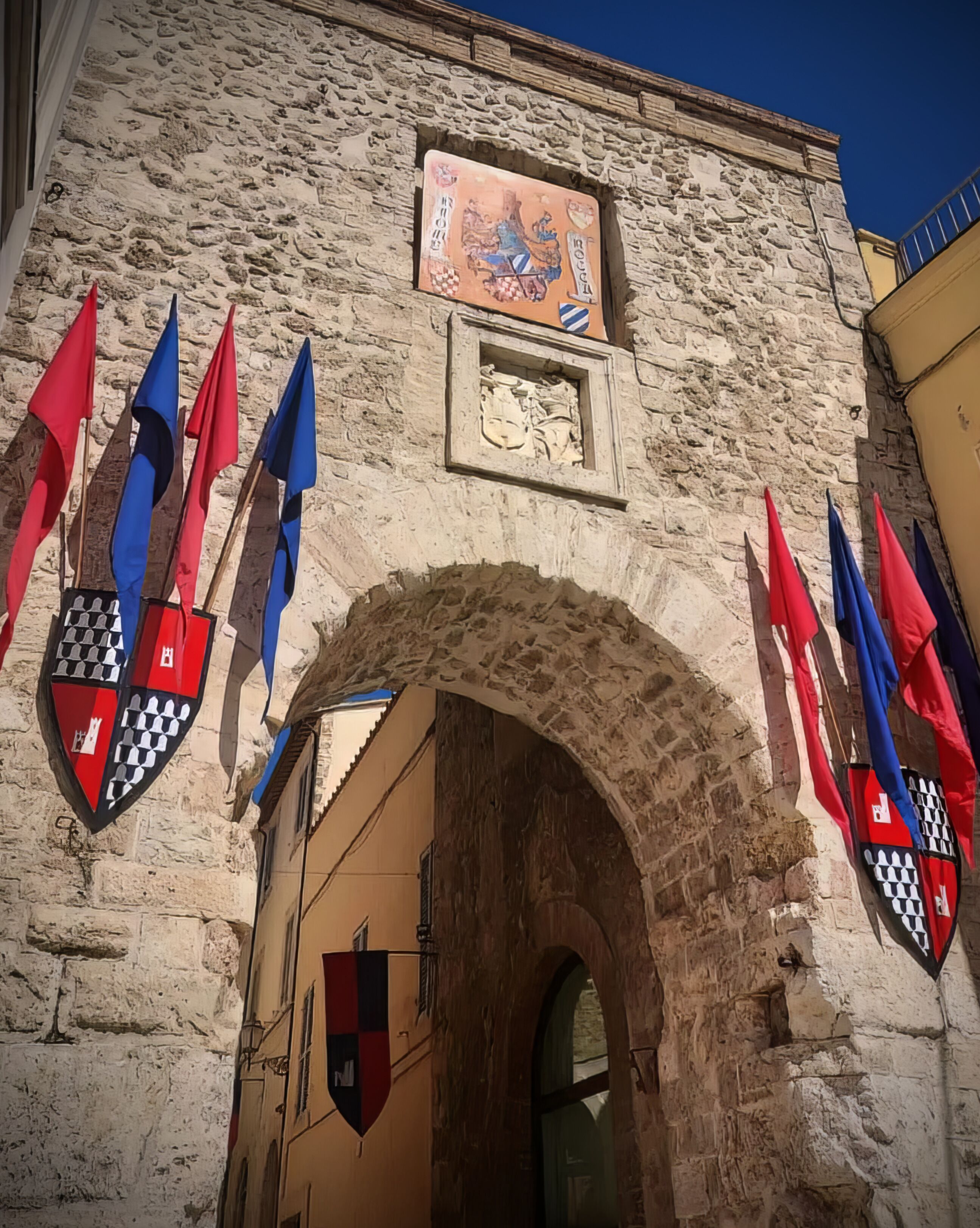 Un edificio de piedra con un amplio arco de entrada, banderas y un escudo de armas.