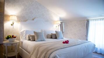 A neatly made bed with a white headboard, two bedside lamps, and a bowl of fruit on a small table beside the bed.