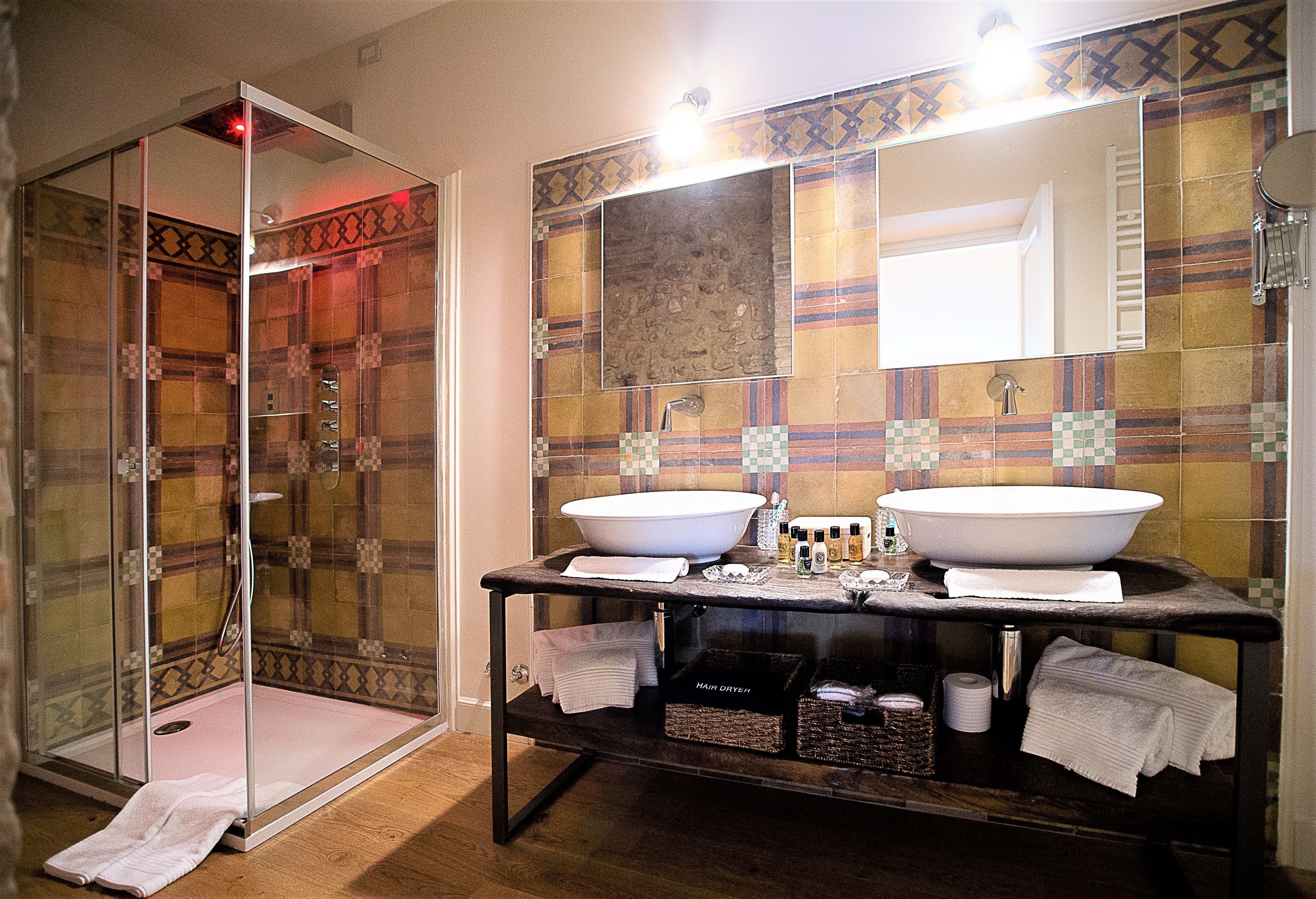 Un baño con dos lavamanos, cabina de ducha de vidrio y salpicadero de azulejos.