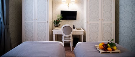 A hotel room with two beds, a desk with a chair, a TV, and a fruit basket.
