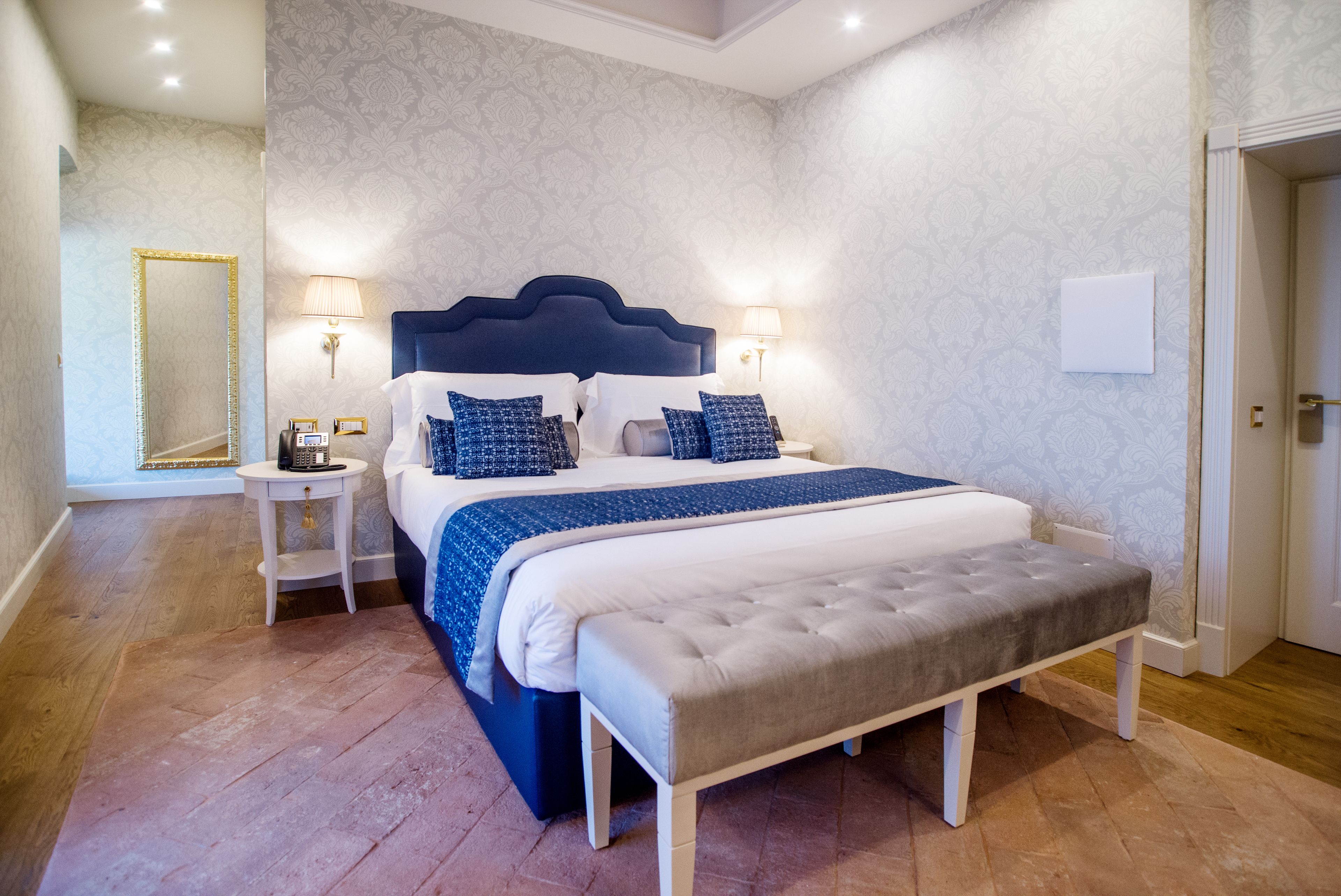 Une chambre à coucher avec un grand lit, deux tables de chevet, un banc et un miroir.