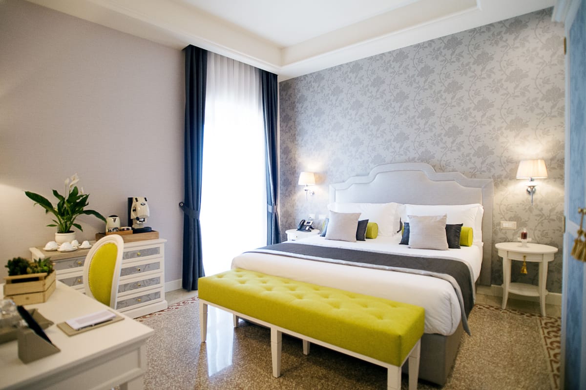Une chambre d’hôtel avec un lit bien fait, un bureau avec une chaise, une petite table et un banc.