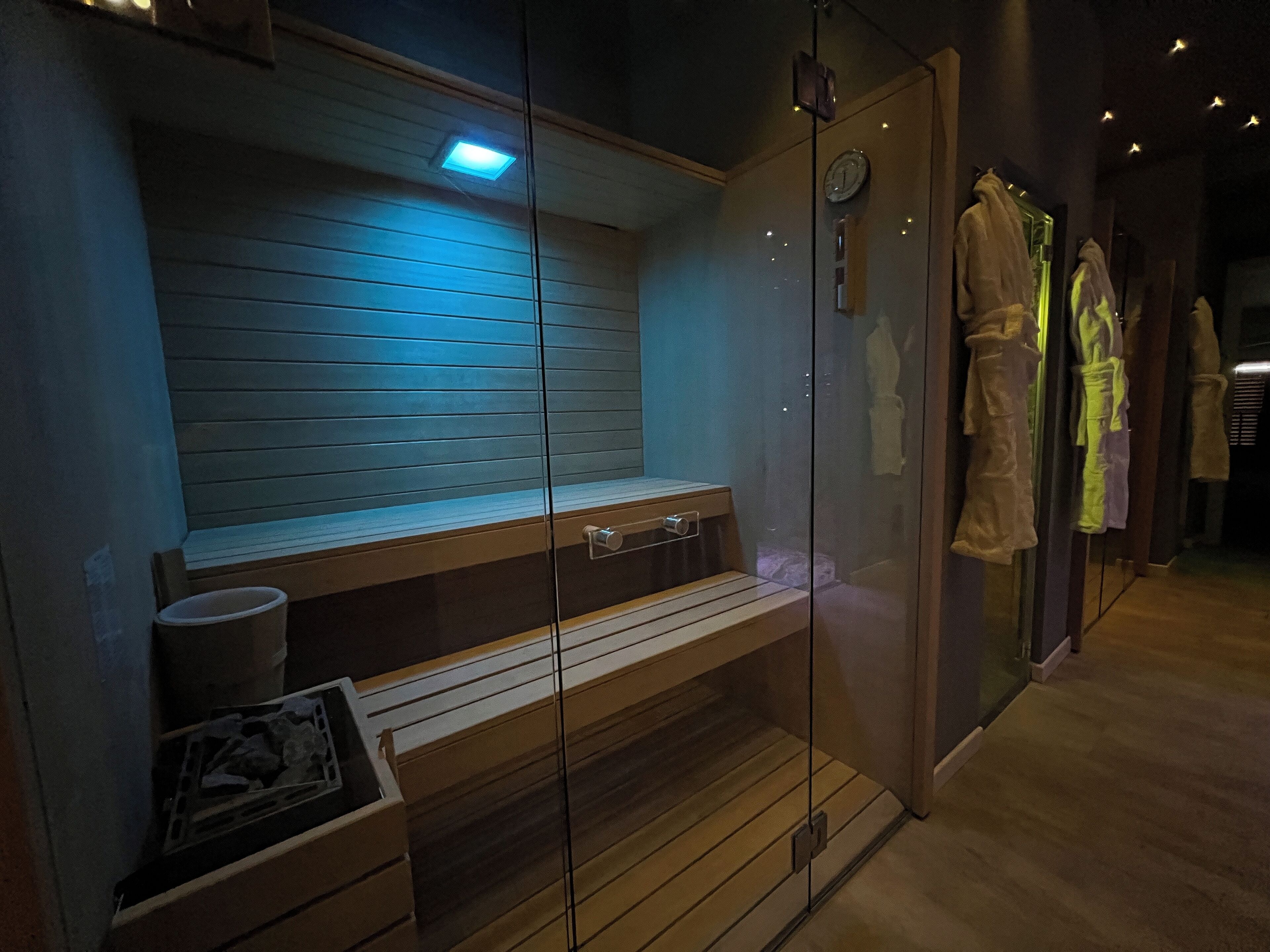 A sauna room with a bench, a glass door, and a clock on the wall.