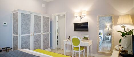 A hotel room with a bed, a desk with a chair, a television, a mirror, and a lamp.