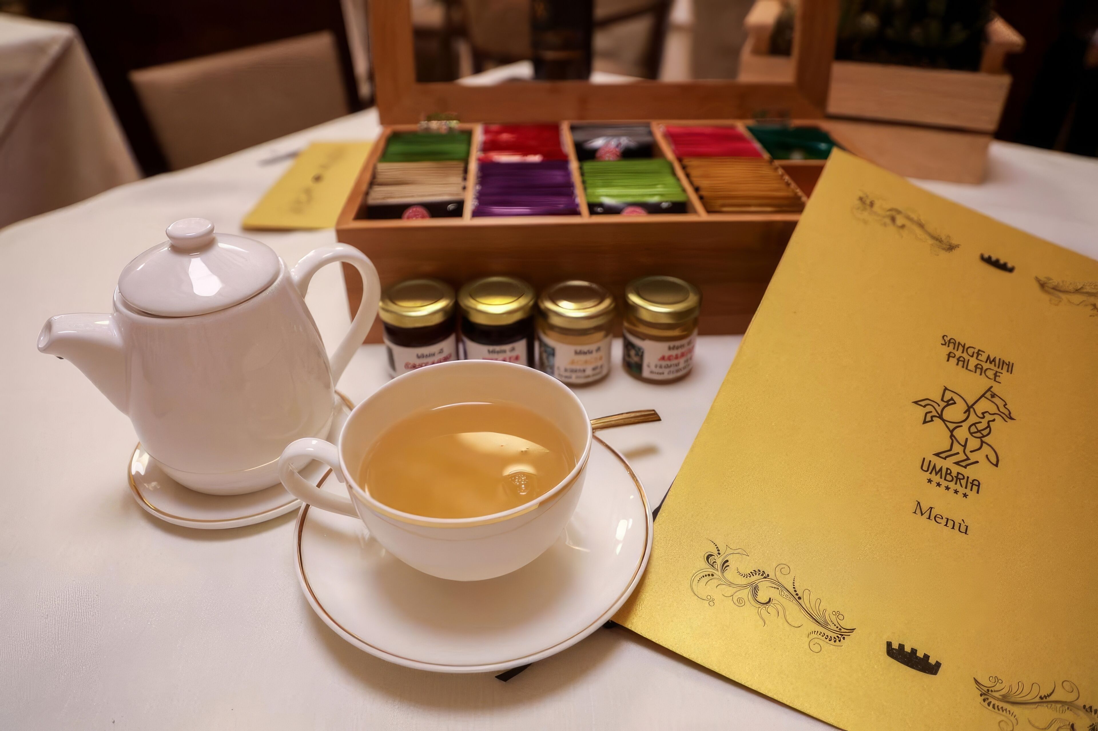 A table with a teapot, a cup of tea, a menu, and a box of tea flavors.